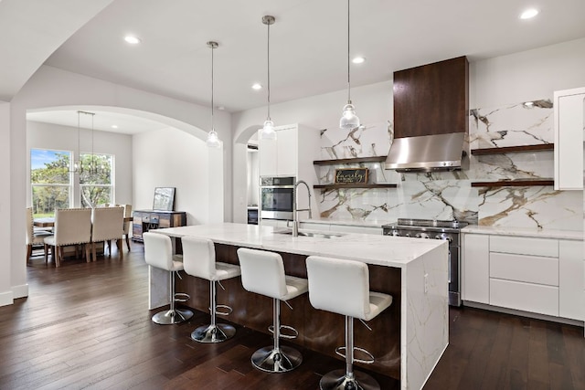 25101 Fawn Dr, Leander, TX 78641 - kitchen featuring open shelves, appliances with stainless steel finishes, wall chimney range hood, arched walkways, and recessed lighting