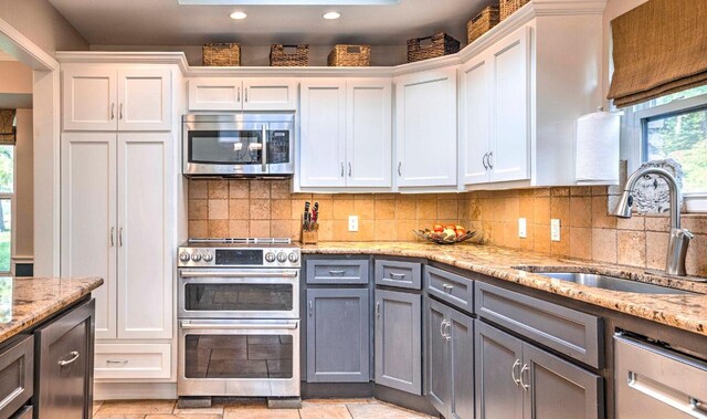 kitchen featuring decorative backsplash, white cabinets, stainless steel appliances, a sink, and gray cabinets