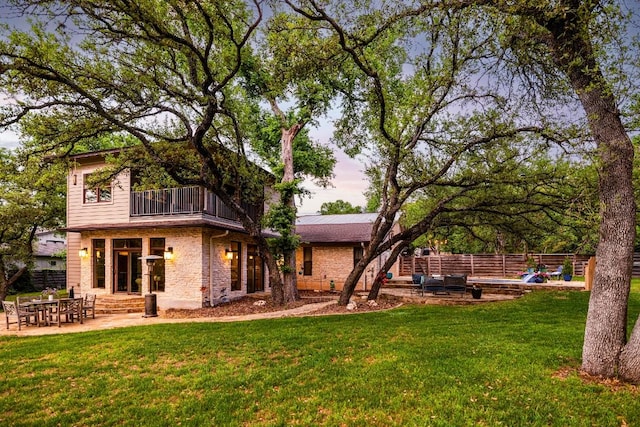 rear view of property with a balcony, a lawn, fence, and a patio area