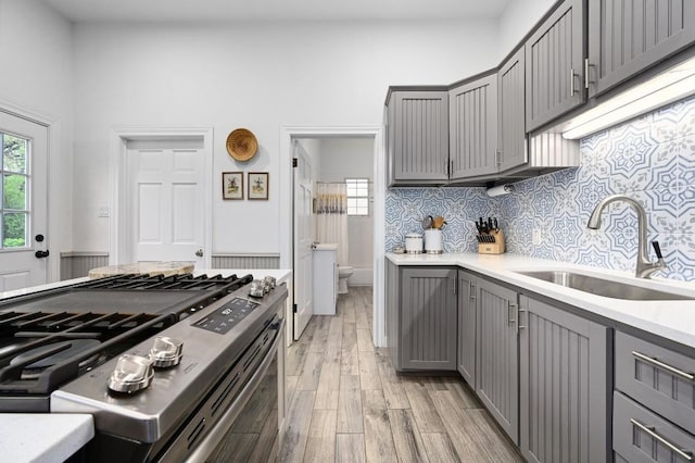 200 Oak Grove Dr, Dripping Springs, TX 78620 - kitchen with stainless steel range with gas stovetop, gray cabinets, light wood finished floors, light countertops, and decorative backsplash