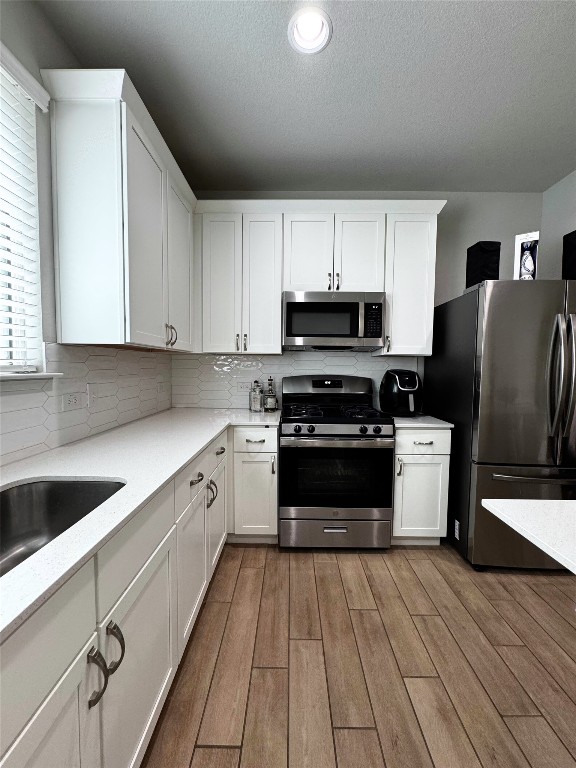 131 Harvest Ridge Blvd, Elgin, TX 78621 - kitchen featuring appliances with stainless steel finishes, wood finished floors, white cabinetry, a textured ceiling, and recessed lighting