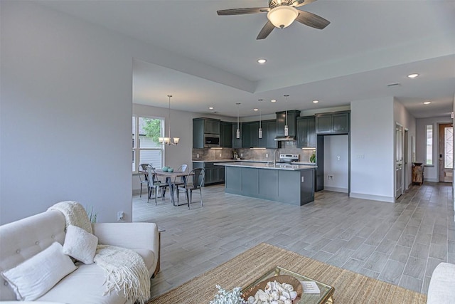 living room with light wood-style flooring, ceiling fan, recessed lighting, a chandelier, and baseboards