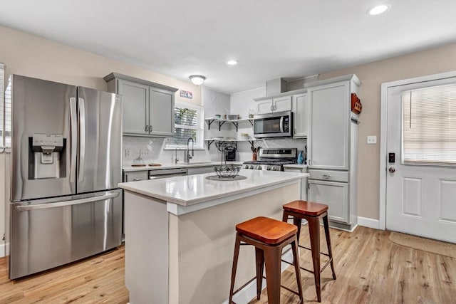 1701 Davis St, Taylor, TX 76574 - kitchen featuring appliances with stainless steel finishes, light wood-type flooring, a breakfast bar, light countertops, and decorative backsplash