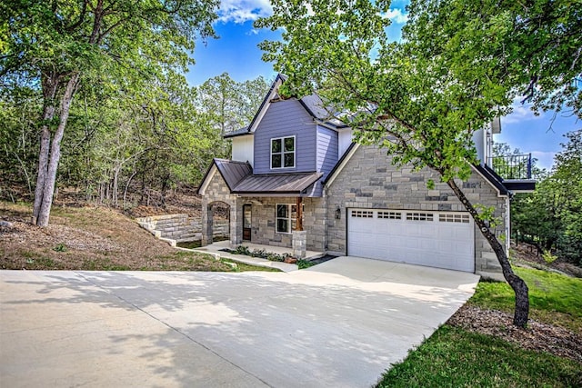 view of front of house featuring stone siding, a garage, a standing seam roof, covered porch, and driveway