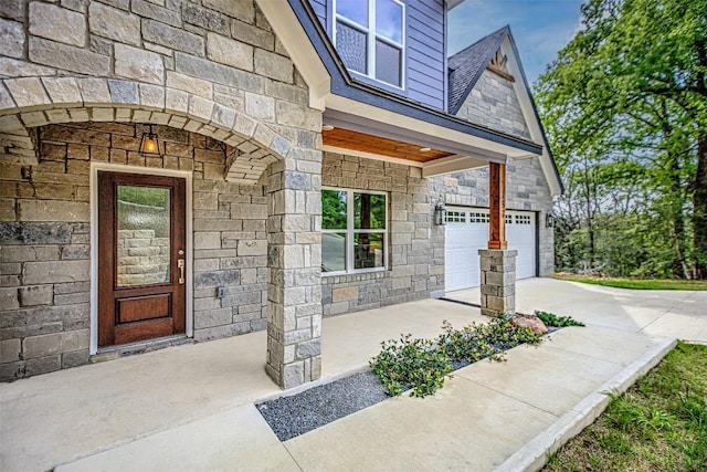 doorway to property featuring concrete driveway, an attached garage, and stone siding