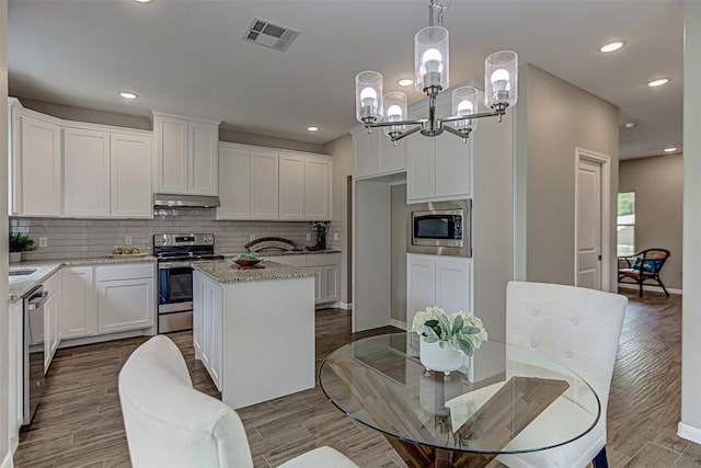 kitchen with visible vents, under cabinet range hood, tasteful backsplash, a chandelier, and stainless steel appliances