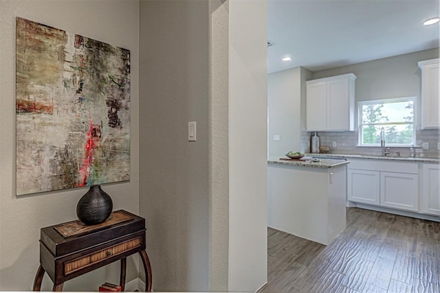 kitchen featuring white cabinets, light stone countertops, a sink, light wood-style floors, and backsplash
