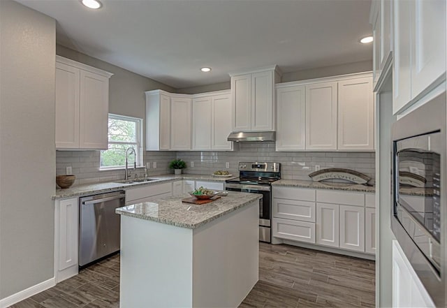 kitchen with a sink, white cabinets, dark wood-style floors, under cabinet range hood, and stainless steel appliances