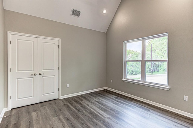 unfurnished bedroom featuring visible vents, a closet, wood finished floors, baseboards, and vaulted ceiling