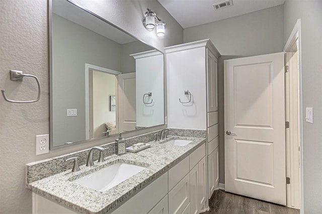 bathroom with a sink, double vanity, wood finished floors, and visible vents