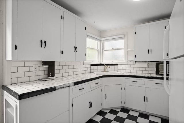 7202 Marcell St, Austin, TX 78752 - kitchen with freestanding refrigerator, white cabinets, backsplash, tile patterned floors, and tile countertops