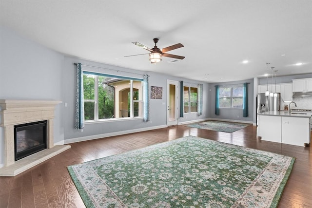 living area with baseboards, a glass covered fireplace, a ceiling fan, and plenty of natural light