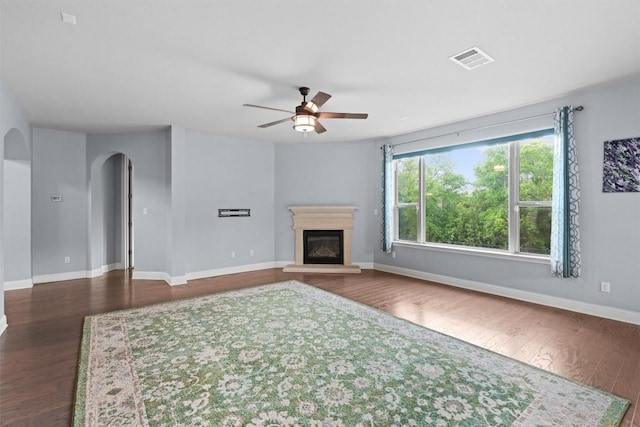 unfurnished living room featuring dark wood finished floors, arched walkways, a glass covered fireplace, baseboards, and a ceiling fan