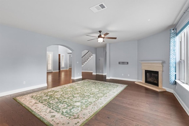 living room featuring stairway, a glass covered fireplace, a ceiling fan, visible vents, and arched walkways