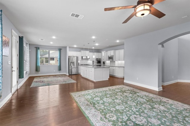 unfurnished living room with visible vents, ceiling fan, dark wood-style floors, baseboards, and arched walkways