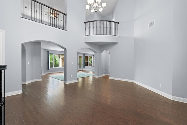 unfurnished living room featuring a chandelier, visible vents, a towering ceiling, arched walkways, and wood finished floors