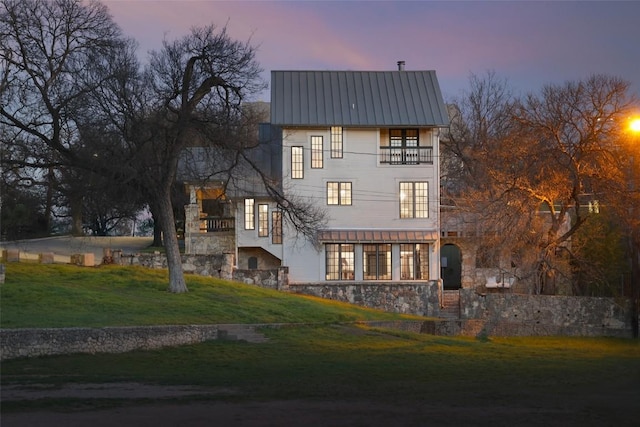 1313 W 9th 1/2 St, Austin, TX 78703 - back of house at dusk featuring a balcony, a yard, a metal roof, and stone siding