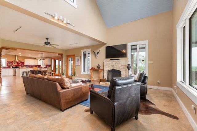 living area with a high ceiling, ceiling fan, baseboards, and a stone fireplace