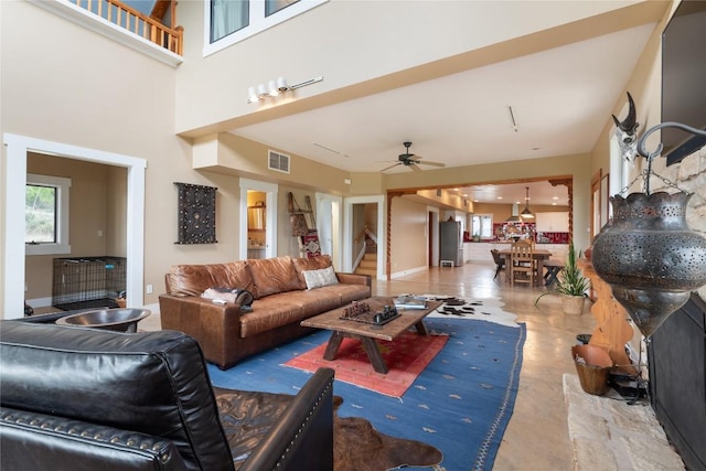 living area featuring ceiling fan, visible vents, stairway, a high ceiling, and baseboards
