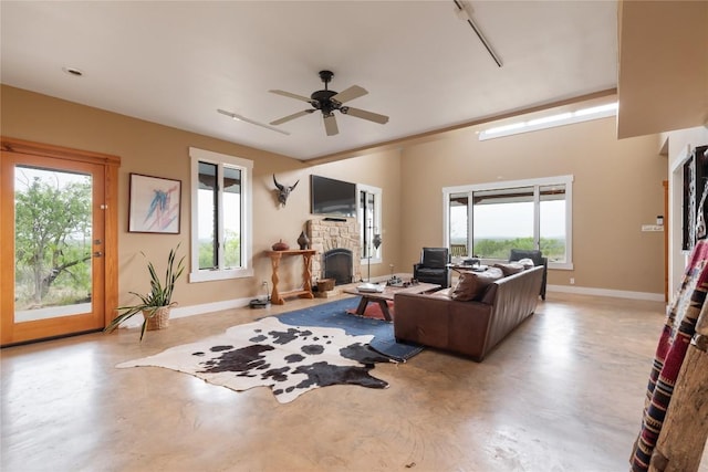 living room with baseboards, a stone fireplace, concrete flooring, and ceiling fan