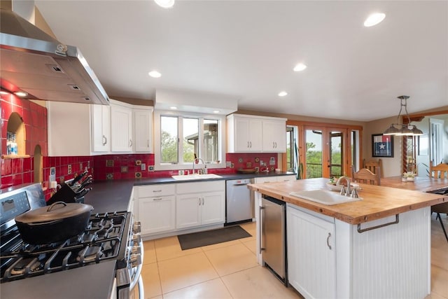 kitchen featuring wall chimney range hood, butcher block counters, a sink, and appliances with stainless steel finishes