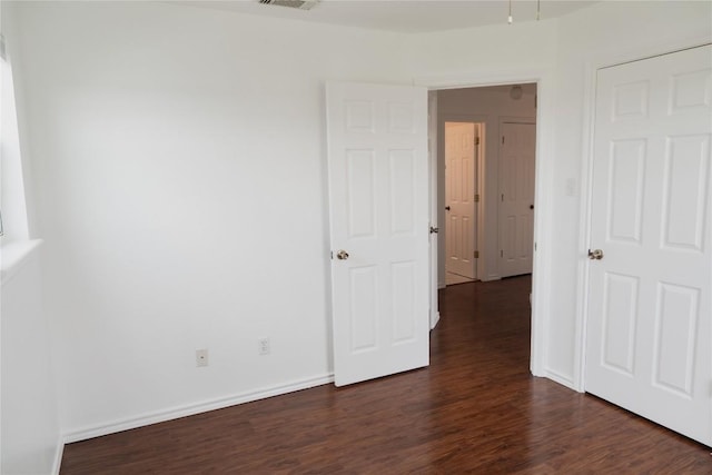 unfurnished bedroom featuring dark wood-style flooring, baseboards, and visible vents