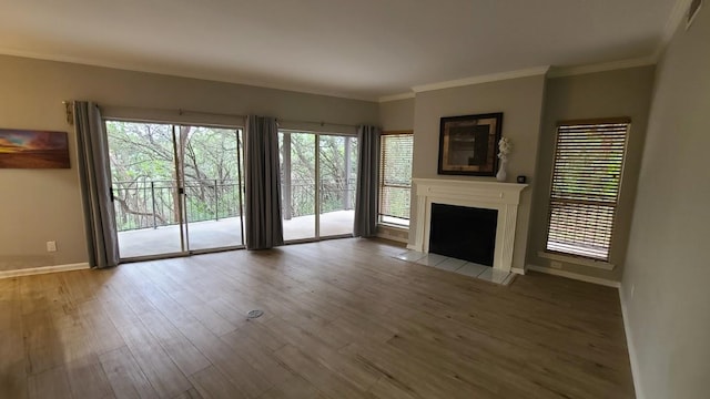 unfurnished living room with wood finished floors, a tiled fireplace, crown molding, and baseboards