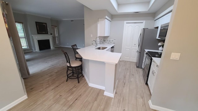kitchen featuring white cabinets, a sink, light wood-style floors, appliances with stainless steel finishes, and a breakfast bar area