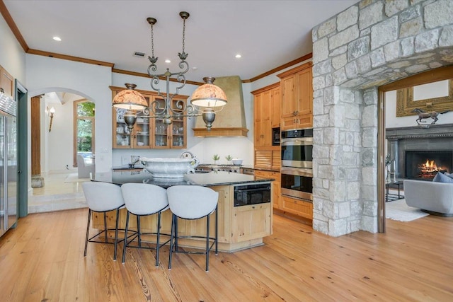 4646 Rockcliff Rd, Austin, TX 78746 - kitchen featuring arched walkways, stainless steel double oven, ornamental molding, custom exhaust hood, and an island with sink