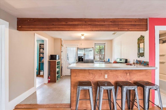 1713 S 5th St, Austin, TX 78704 - kitchen with stainless steel fridge, beamed ceiling, a peninsula, a kitchen breakfast bar, and light countertops