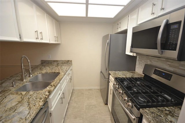 kitchen featuring light stone counters, a sink, white cabinetry, tasteful backsplash, and appliances with stainless steel finishes