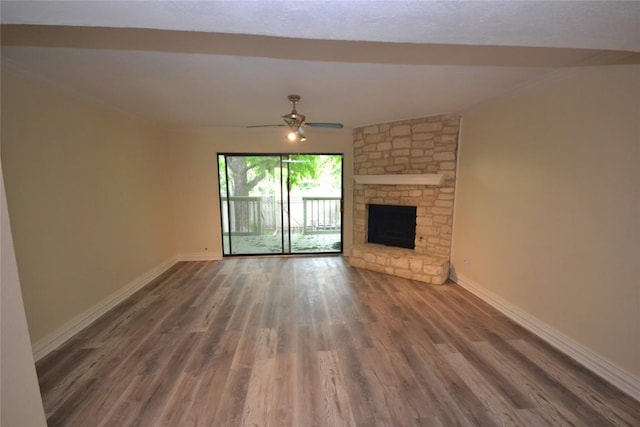 unfurnished living room with a ceiling fan, a stone fireplace, baseboards, and wood finished floors