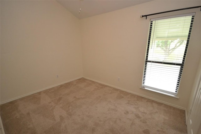 spare room featuring light colored carpet, lofted ceiling, and baseboards