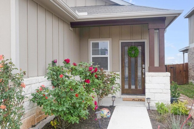 doorway to property featuring board and batten siding, fence, and a shingled roof