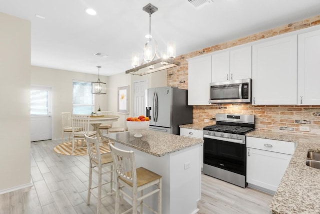 kitchen with an inviting chandelier, light wood-style flooring, tasteful backsplash, a center island, and appliances with stainless steel finishes