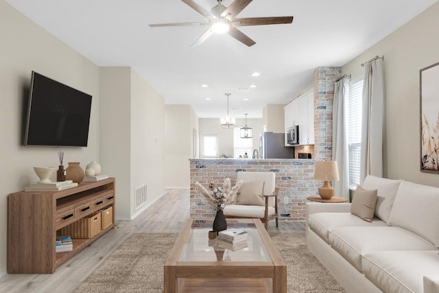 living room featuring light wood-style floors, ceiling fan, visible vents, and a wealth of natural light