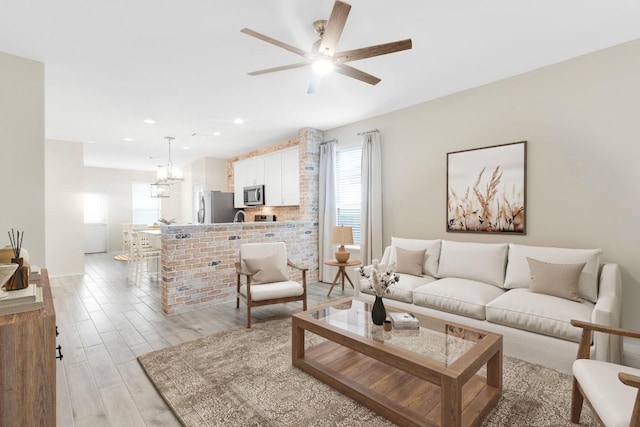 living area featuring light wood-style floors, ceiling fan with notable chandelier, baseboards, and recessed lighting