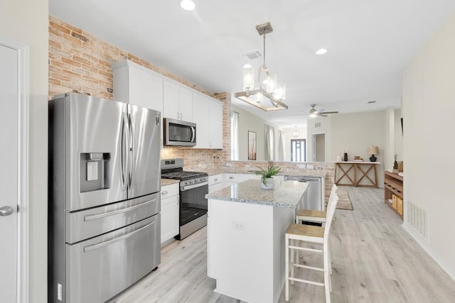 kitchen with a peninsula, white cabinetry, appliances with stainless steel finishes, light wood finished floors, and ceiling fan with notable chandelier