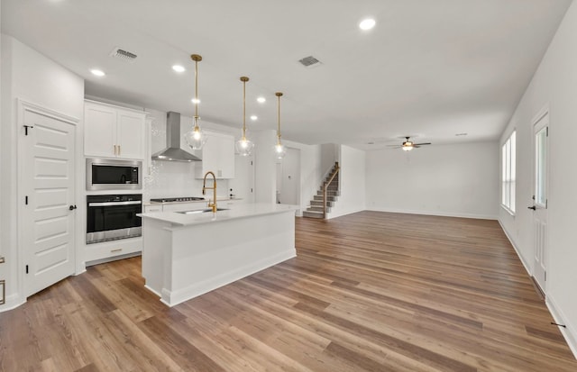 16724 Santiaguillo Trce, Manor, TX 78653 - kitchen featuring stainless steel appliances, wall chimney exhaust hood, ceiling fan, a center island with sink, and white cabinets