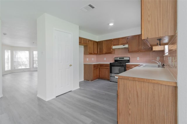 15406 Ecorio Dr, Austin, TX 78728 - kitchen with stainless steel gas stove, under cabinet range hood, light wood finished floors, light countertops, and backsplash