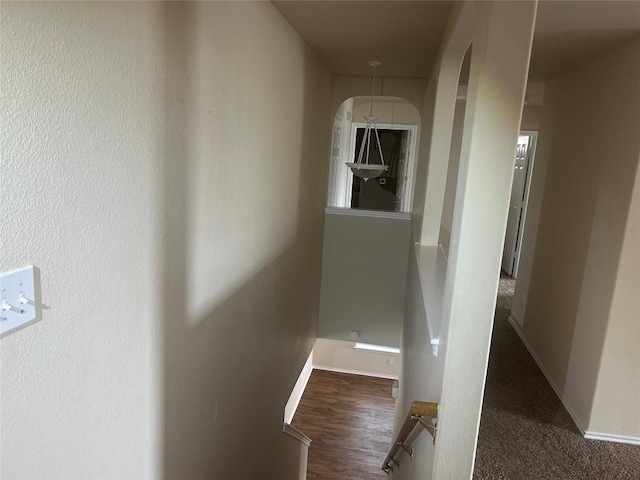 hallway featuring arched walkways, baseboards, and wood finished floors
