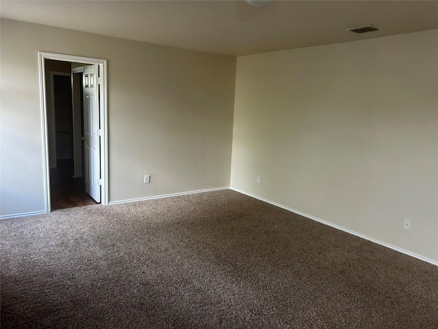 empty room featuring dark carpet, visible vents, and baseboards
