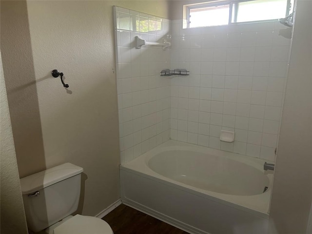 full bathroom featuring baseboards, toilet, a textured wall, wood finished floors, and bathing tub / shower combination