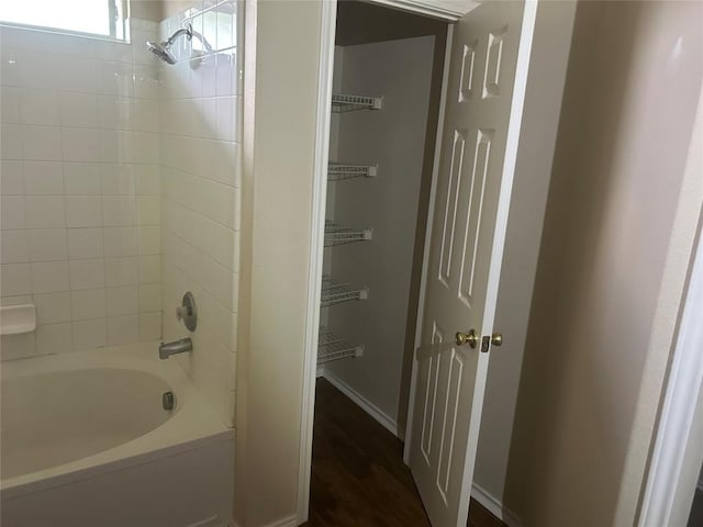 full bath featuring wood finished floors, baseboards, and washtub / shower combination