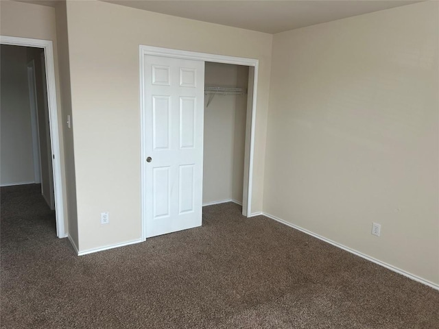 unfurnished bedroom featuring dark carpet, a closet, and baseboards