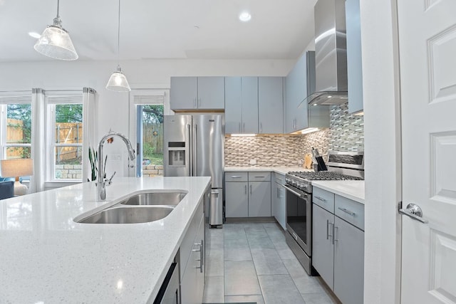 kitchen with light tile patterned floors, gray cabinetry, wall chimney exhaust hood, stainless steel appliances, and a sink