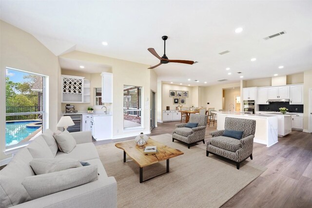 8316 Talbot Ln, Austin, TX 78746 - living room featuring light wood-style flooring, beverage cooler, ceiling fan, bar, and recessed lighting