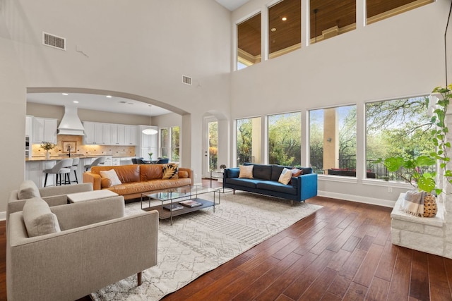 living area with arched walkways, dark wood finished floors, baseboards, visible vents, and a high ceiling