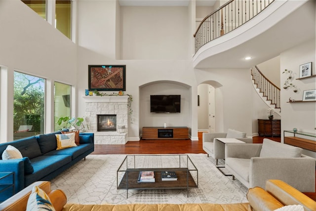 living area featuring stairway, a towering ceiling, wood finished floors, baseboards, and a fireplace