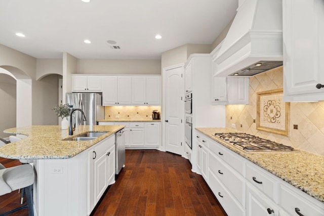 kitchen with light stone counters, custom exhaust hood, white cabinets, stainless steel appliances, and dark wood finished floors
